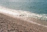 Crystal-clear waters gently washing over smooth pebbles on a quiet Greek beach.