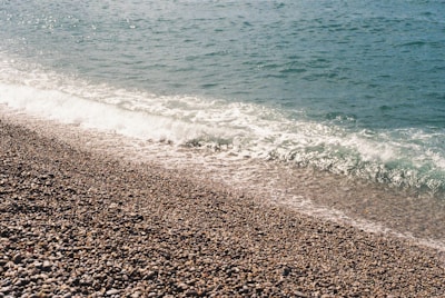 Crystal-clear waters gently washing over smooth pebbles on a quiet Greek beach.