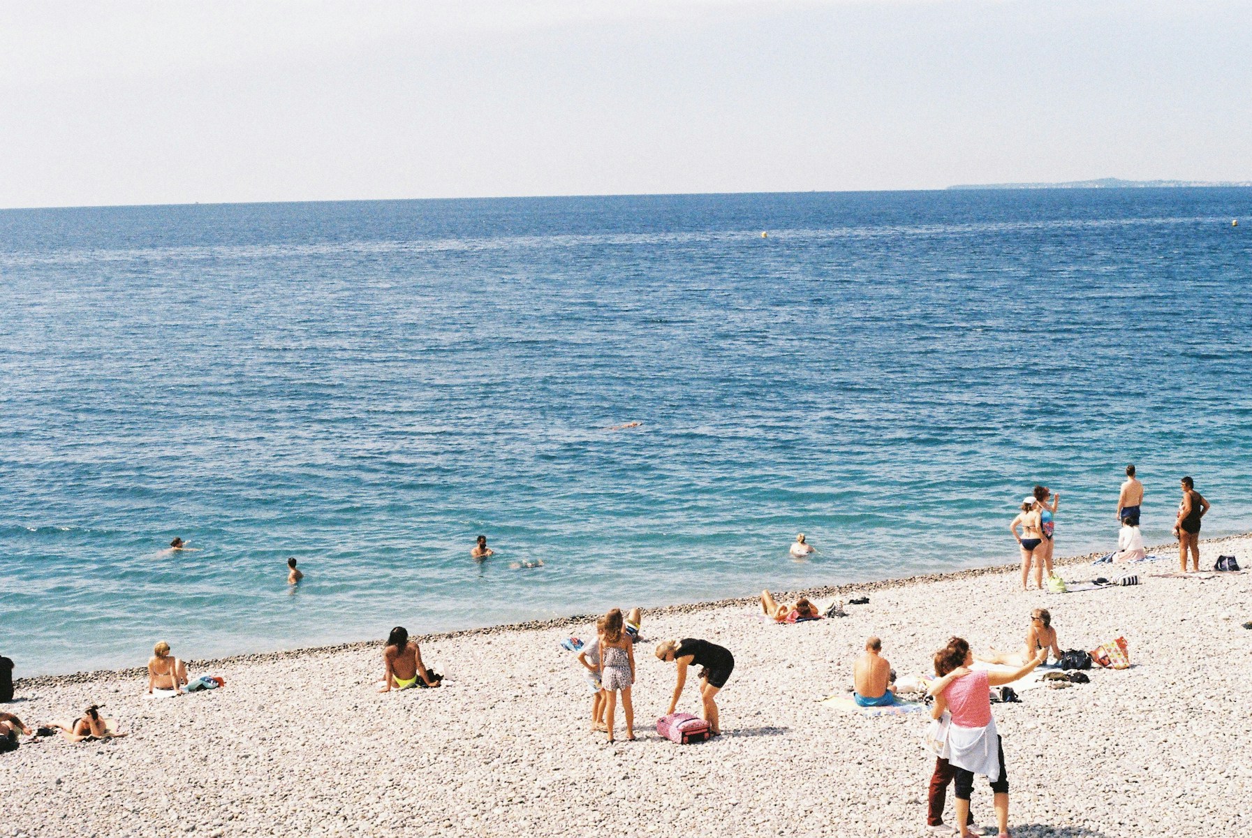 Swimmers and sunbathers on a pebble beach under a clear sky