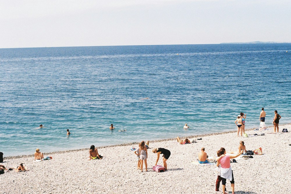 Swimmers and sunbathers on a pebble beach under a clear sky