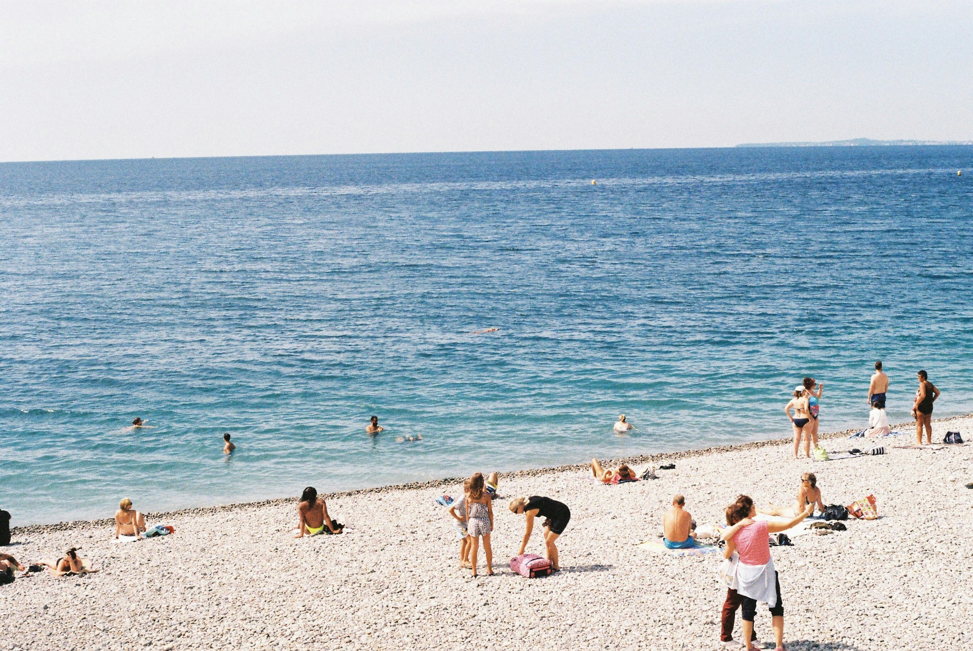 Swimmers and sunbathers on a pebble beach under a clear sky