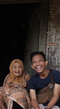 A candid photo of a filmmaker interviewing a community elder in a sunlit village setting.