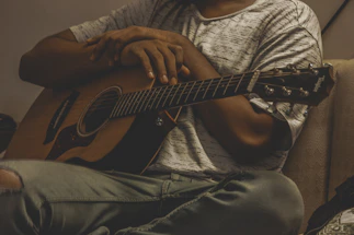 A smiling guitar player holding an acoustic guitar in a warm, cozy setting.