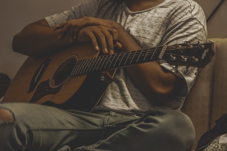 A relaxed guitar tutor demonstrating chord shapes to a smiling student in a cozy home studio.