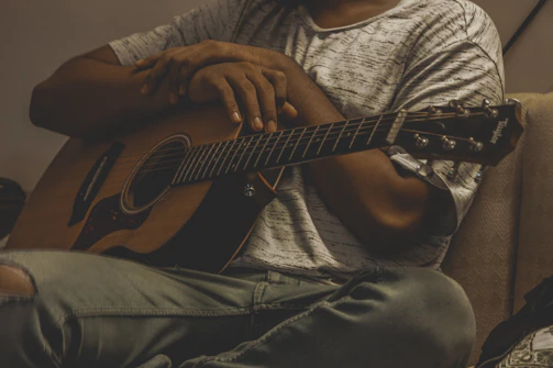 A smiling guitar player holding an acoustic guitar in a warm, cozy setting.