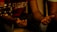 A close-up of hands gesturing with slightly open palms, alongside a part of an acoustic guitar. The scene is warmly lit, focusing on the expressive body language.