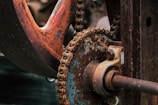 Close-up view of a rusty mechanical gear system with a chain and bolted components, showing signs of wear and age.