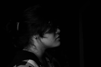 A black and white profile photograph captures a young woman with her hair tied back. She appears to be looking forward against a dark background, wearing a plaid shirt and an earring.