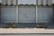 Metal shutters cover the entrance of a building labeled 'TRIBUNAL D'INSTANCE JURIDICTION DE PROXIMITÉ'. Red graffiti with the phrase 'NIQUE LE JUGE' is sprayed on one of the shutters. Two concrete planters with sparse greenery are placed on either side. The ground is paved with cobblestones.