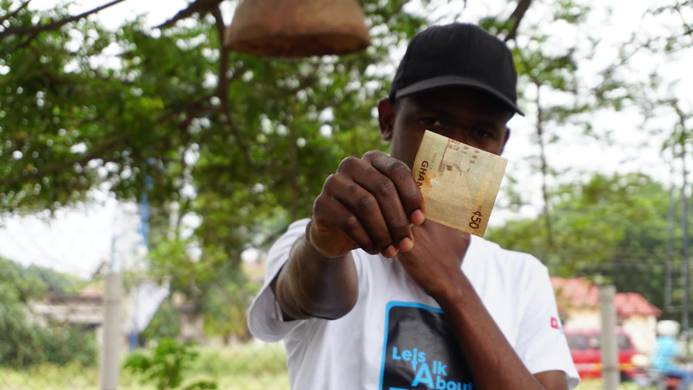 A Ghanaian man holding cedi banknotes
