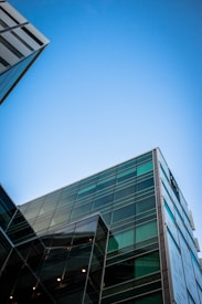 Modern glass-fronted buildings with reflective surfaces stretch upwards into a clear blue sky, showcasing an architectural focus on sleek lines and transparency.