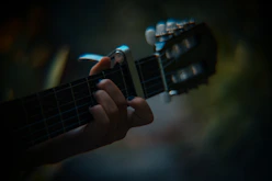 Close-up of hands playing an acoustic guitar with sheet music in soft blue and white tones.