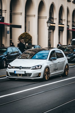 Elegant silver Volkswagen driving through a historic village square under soft sunlight.