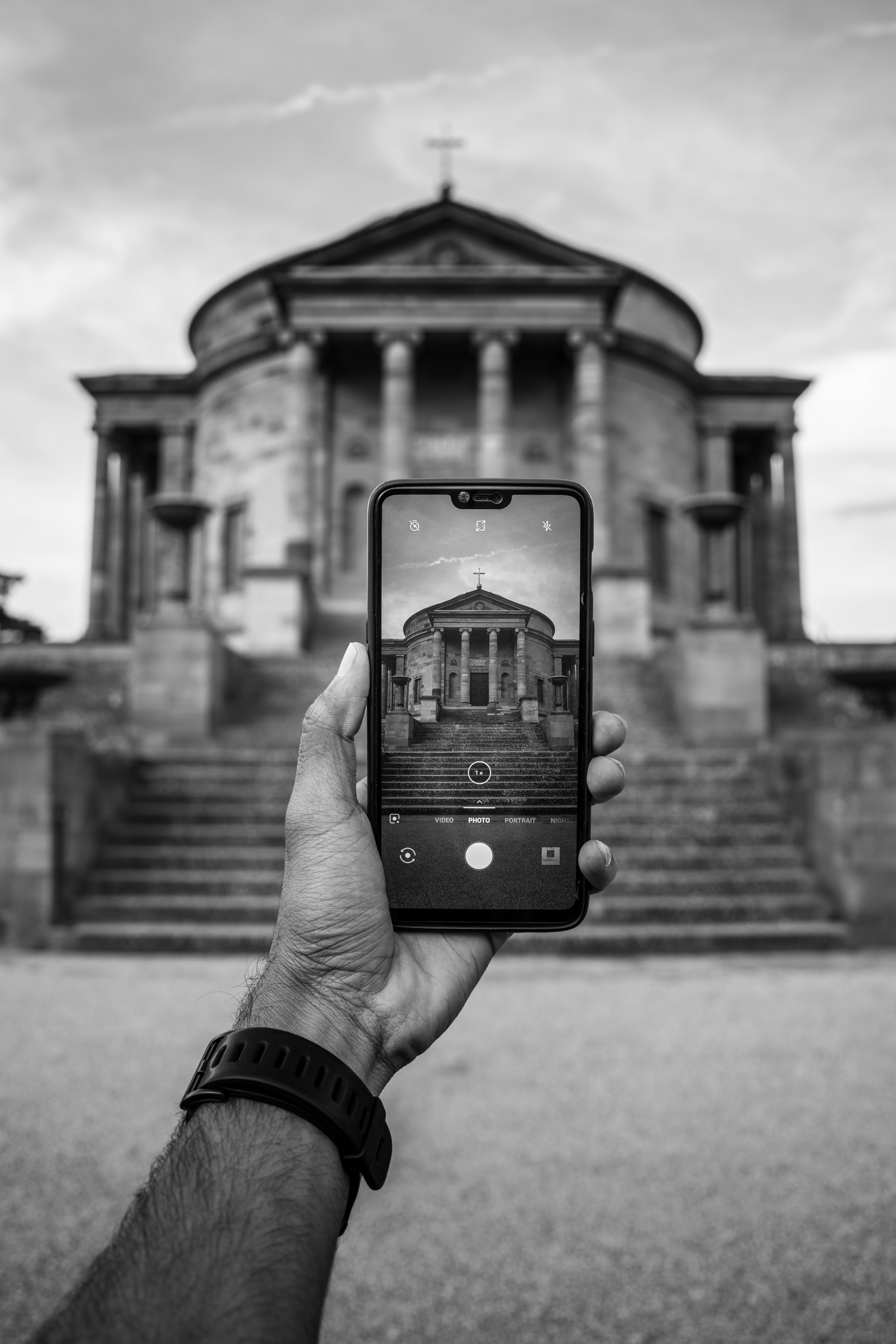 greyscale photo of person taking photo of cathedral with smartphone