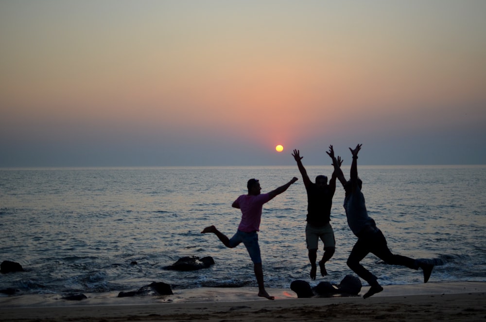 three people jumping on the beach at sunset