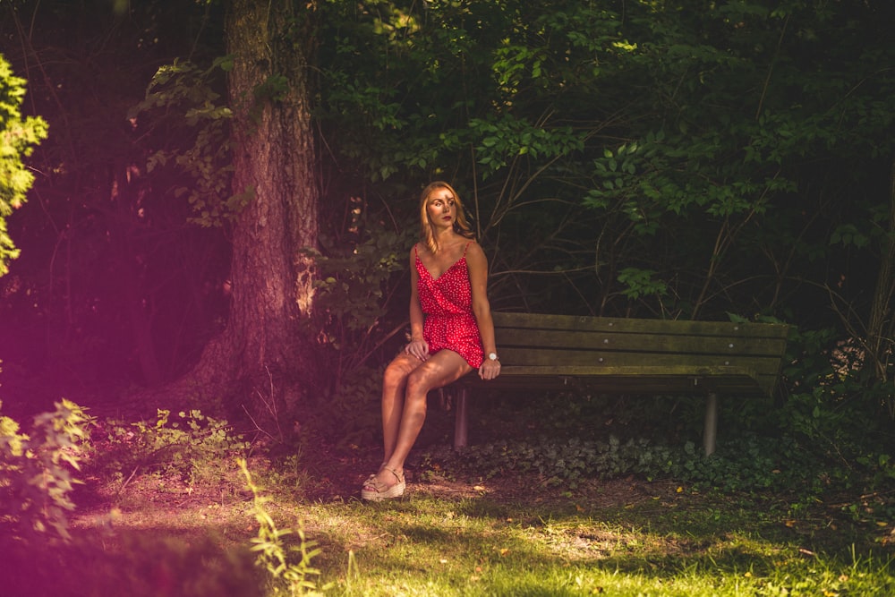 woman sitting on wooden bench surrounded with tall and green trees