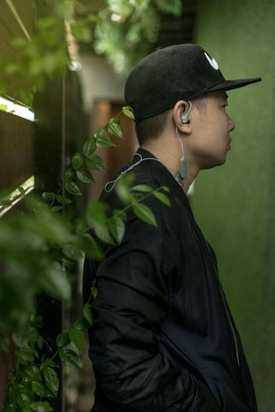 man standing beside leaves and near wall