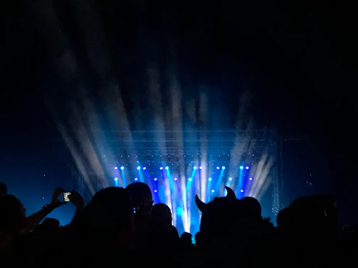 Fans swaying and clapping along under the night sky, illuminated by electric blue stage lights.