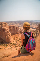 sitting woman carrying backpack overlooking canyon during daytime