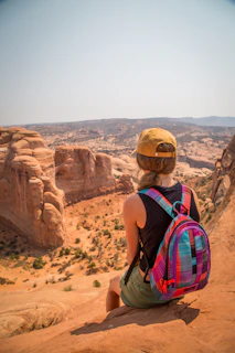 sitting woman carrying backpack overlooking canyon during daytime
