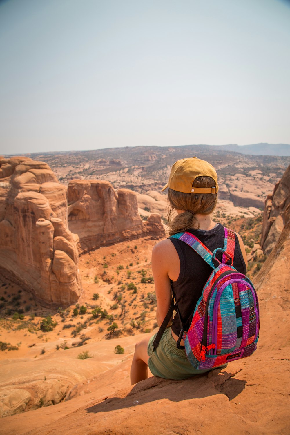 sitting woman carrying backpack overlooking canyon during daytime