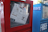 A newspaper vending machine painted red and containing a visible newspaper titled 'SFist' is partly obscured by a sticker. The machine is positioned next to a blue vending machine labeled 'Free Real Estate'. Both machines have a slightly worn appearance, with scratches and minor damage.