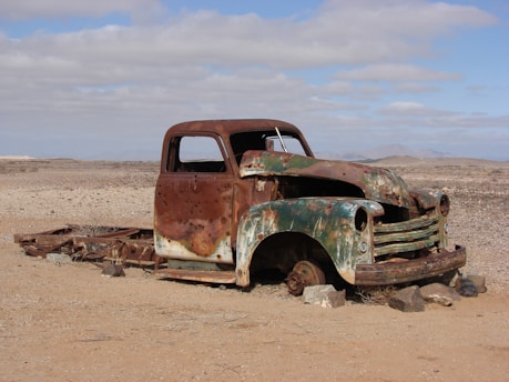 green rusted classic truck lying on desert without wheels