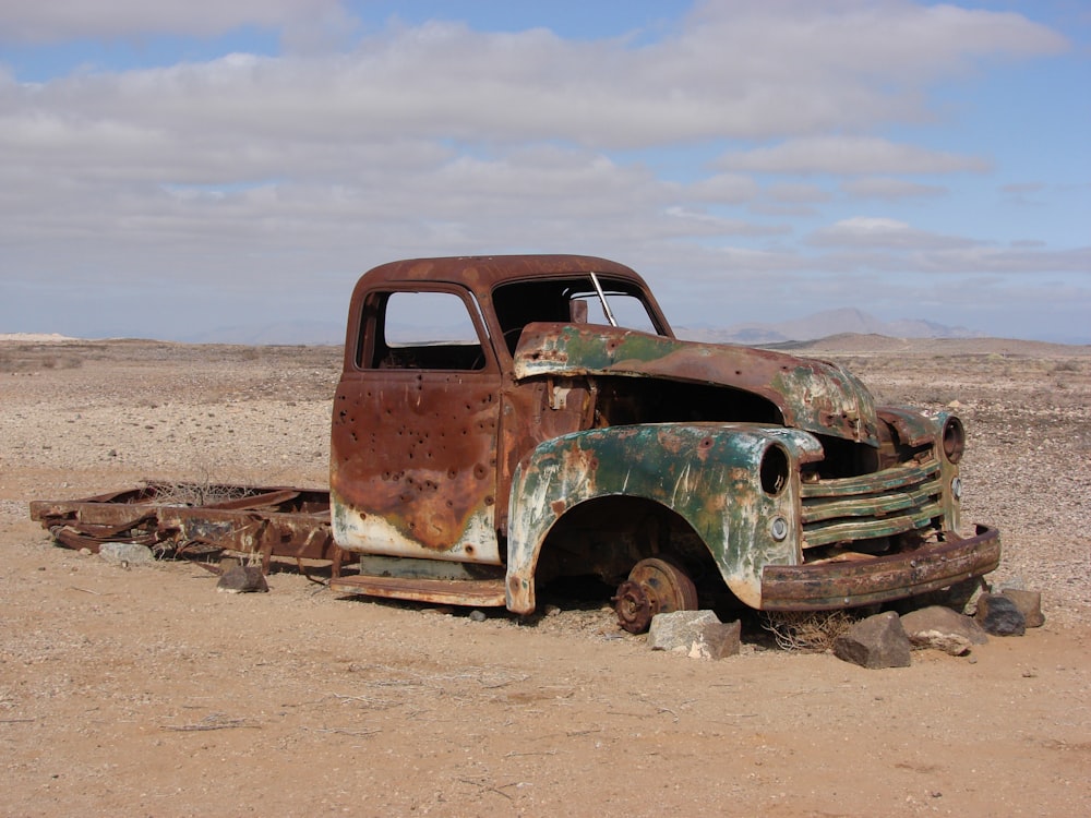 green rusted classic truck lying on desert without wheels