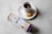 A white cup filled with tea sits on a matching saucer. Next to the cup is a piece of honeycomb. A rectangular package labeled 'honeycomb' is also visible on the table surface, which has a light, textured appearance.