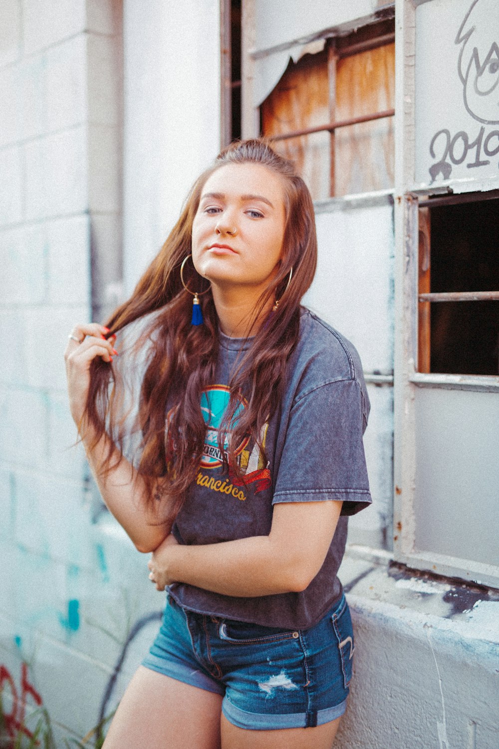 selective focus photography of woman wearing gray t-shirt touching hair leaning on wall