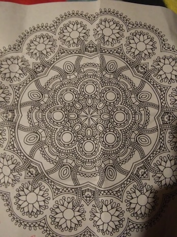 A detailed black and white mandala pattern featuring symmetrical, intricate designs with floral and geometric elements, centered on a piece of paper.