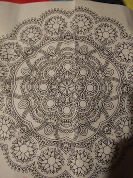 A detailed black and white mandala pattern featuring symmetrical, intricate designs with floral and geometric elements, centered on a piece of paper.