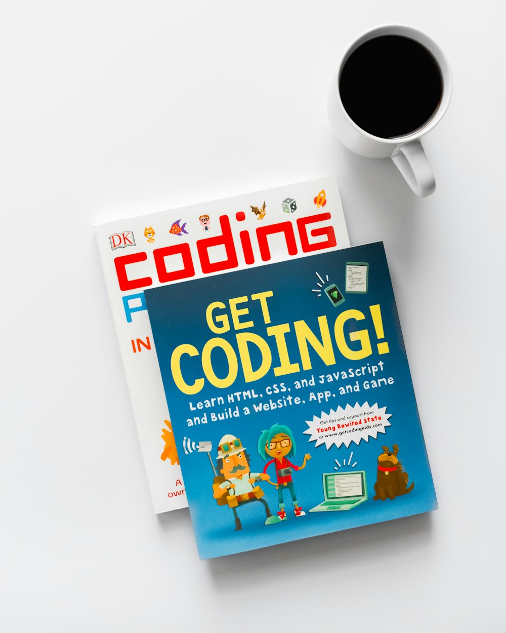 Get Coding and Coding books beside cup of coffee