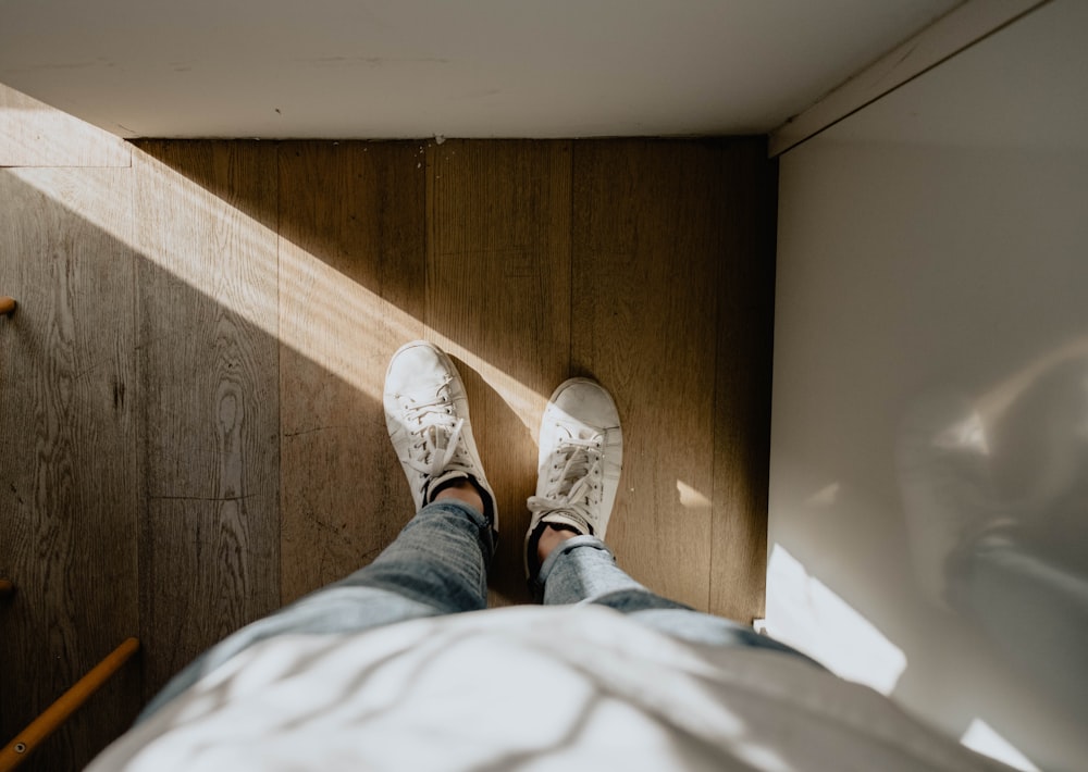 person wearing pair of white shoes standing on brown wood parquet floor