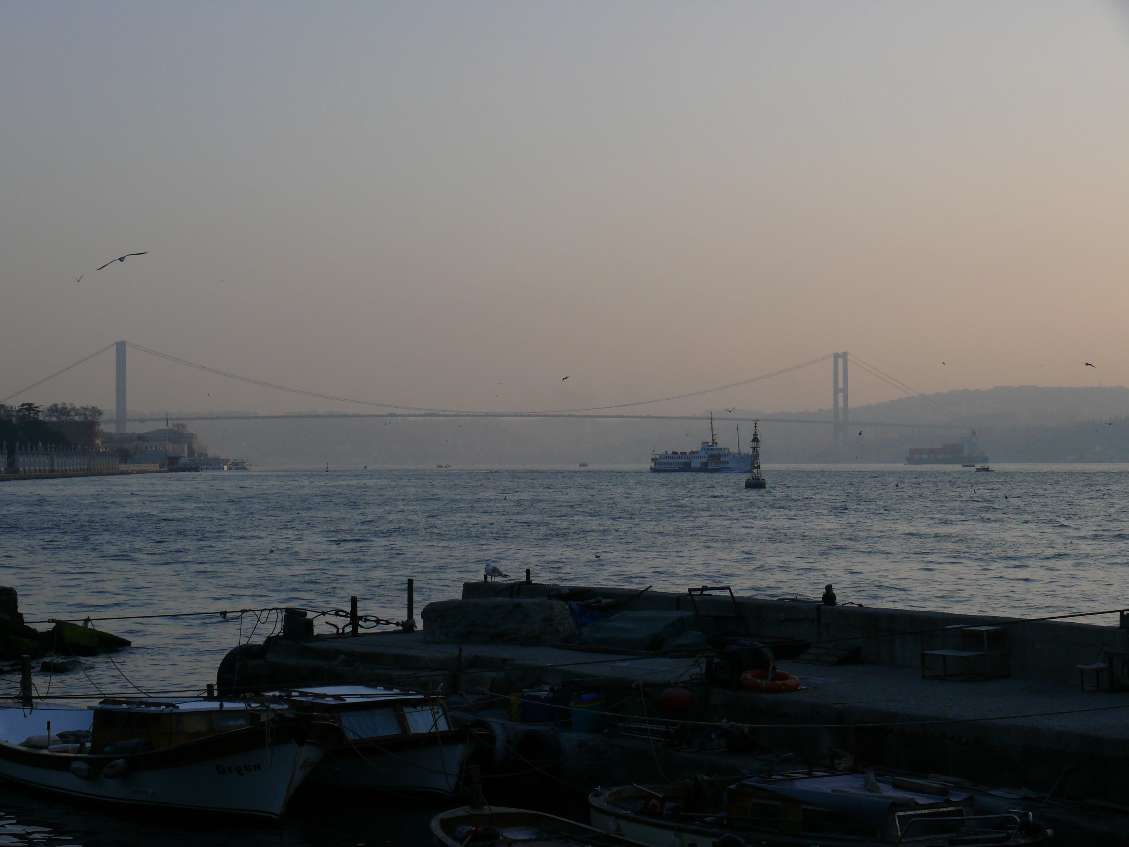 A still morning on the Bosphorus: fishing boats at a quay, a ferry and a suspension bridge in the haze