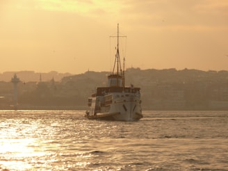 A ship navigating through calm waters with a sunset backdrop.