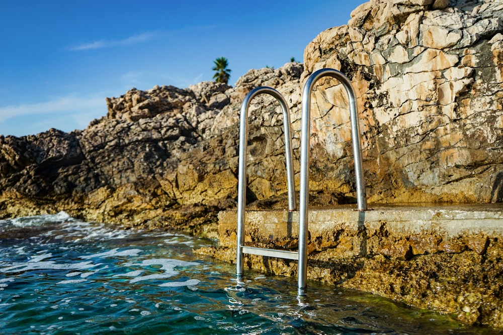 Escalera de piscina de acero inoxidable gris cerca de rocas