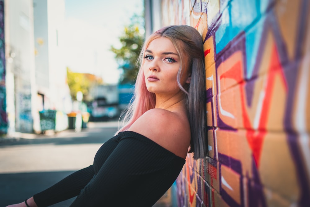 woman in black off-shoulder top leaning on wall