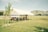 A registration tent set up in a grassy field with a clear sky and mountains in the background. A small group of people, including adults and children, are gathered under the white tent, which has a 'REGISTRATION' sign attached to it.