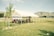 A registration tent set up in a grassy field with a clear sky and mountains in the background. A small group of people, including adults and children, are gathered under the white tent, which has a 'REGISTRATION' sign attached to it.