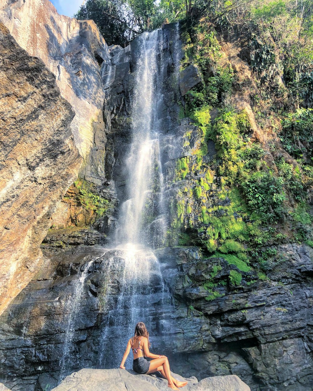 woman sitting on rock boulder in front of waterfall