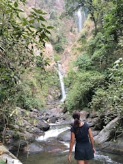 woman walking on river towards waterfalls