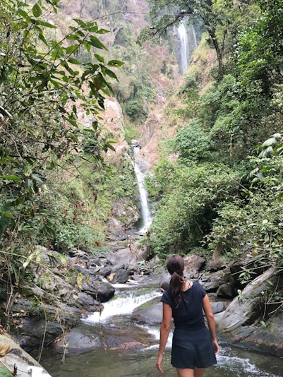 woman walking on river towards waterfalls