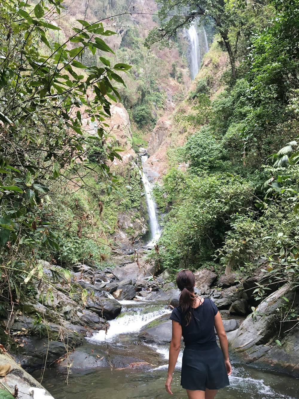 woman walking on river towards waterfalls