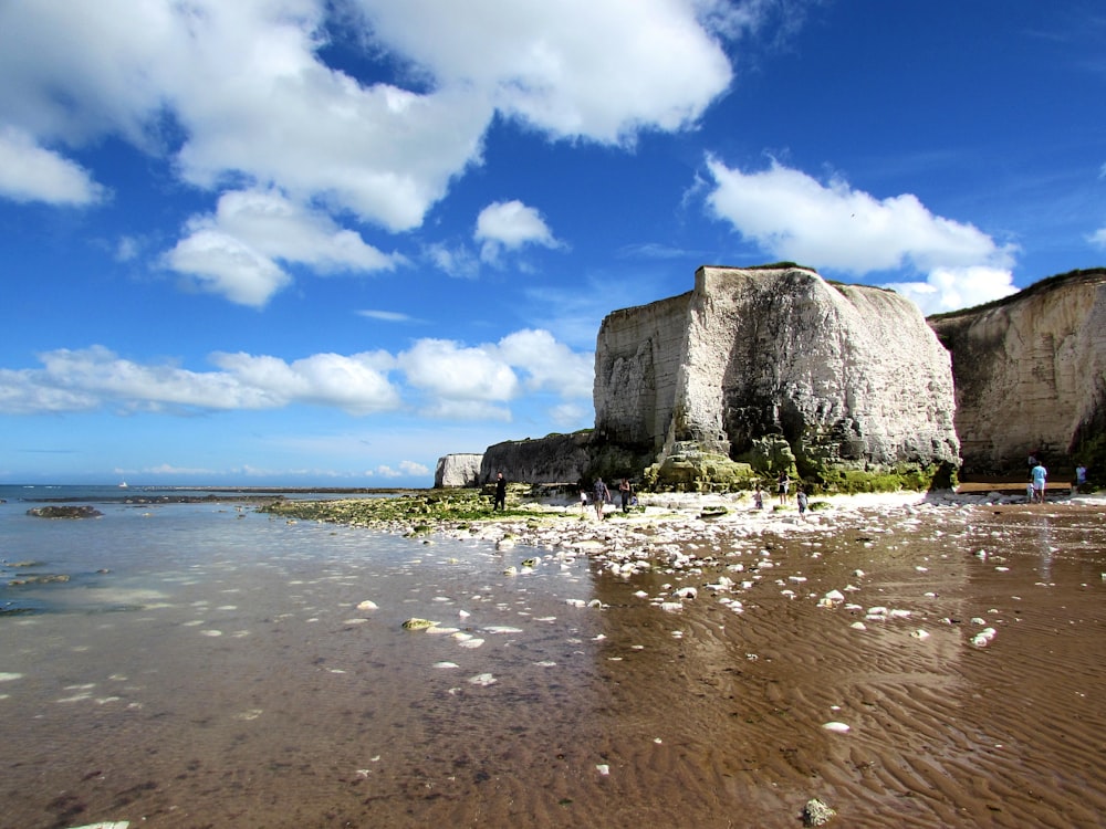 cliff near body of water under white clouds and blue sky during daytime