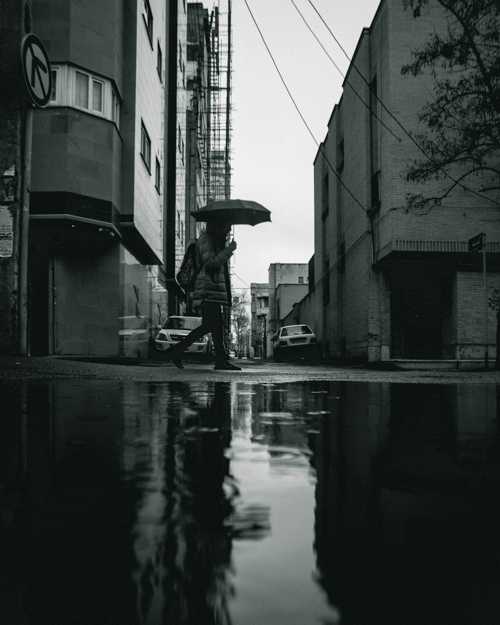 greyscale photo of person walking and holding umbrella