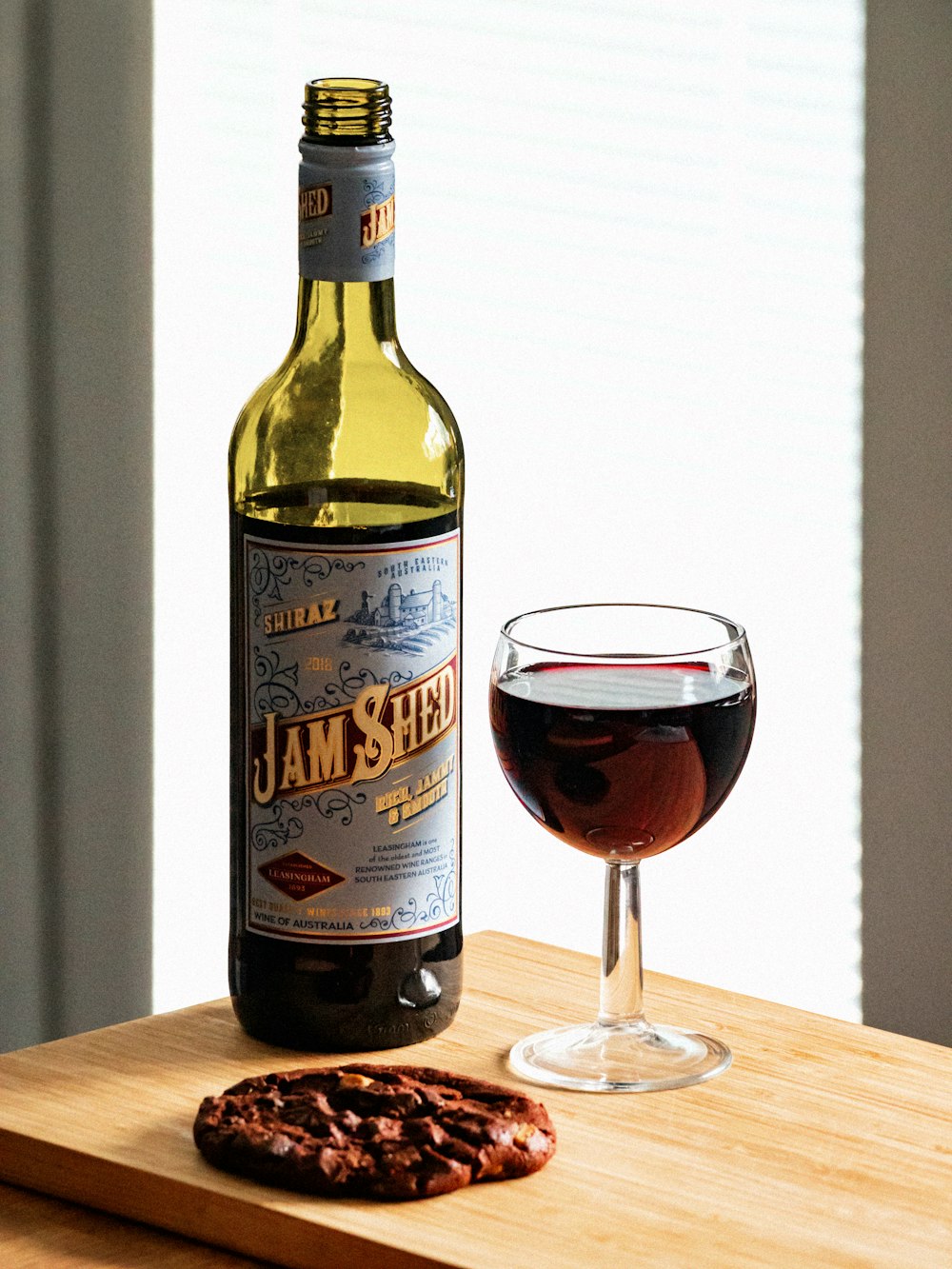 Jam Shed wine bottle beside wine filled wineglass on wooden surface