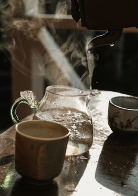 A gentle stream of hot water pouring into a glass teapot, steam curling upwards in soft tendrils.