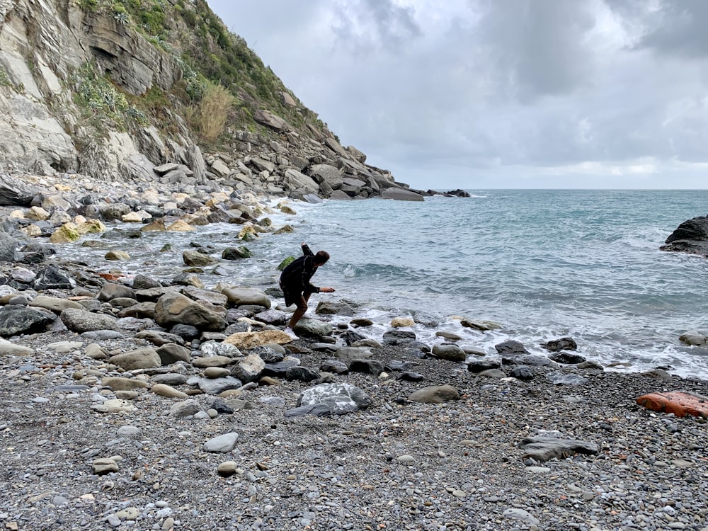 Person, die tagsüber auf einem Felsen am Meeresufer steht