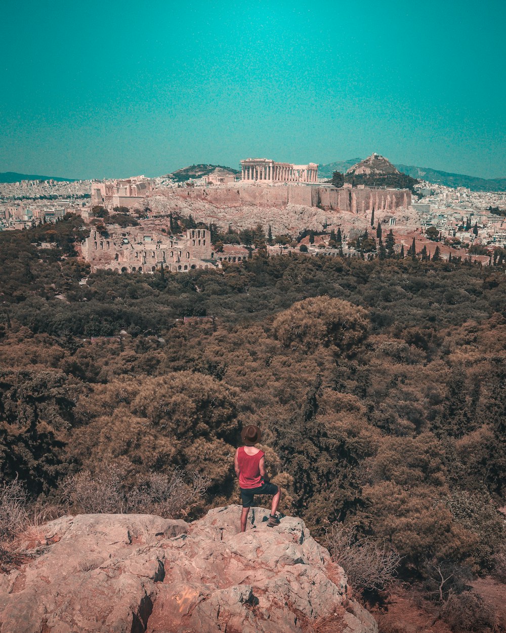 person wearing red tank top standing on top of rock across forest